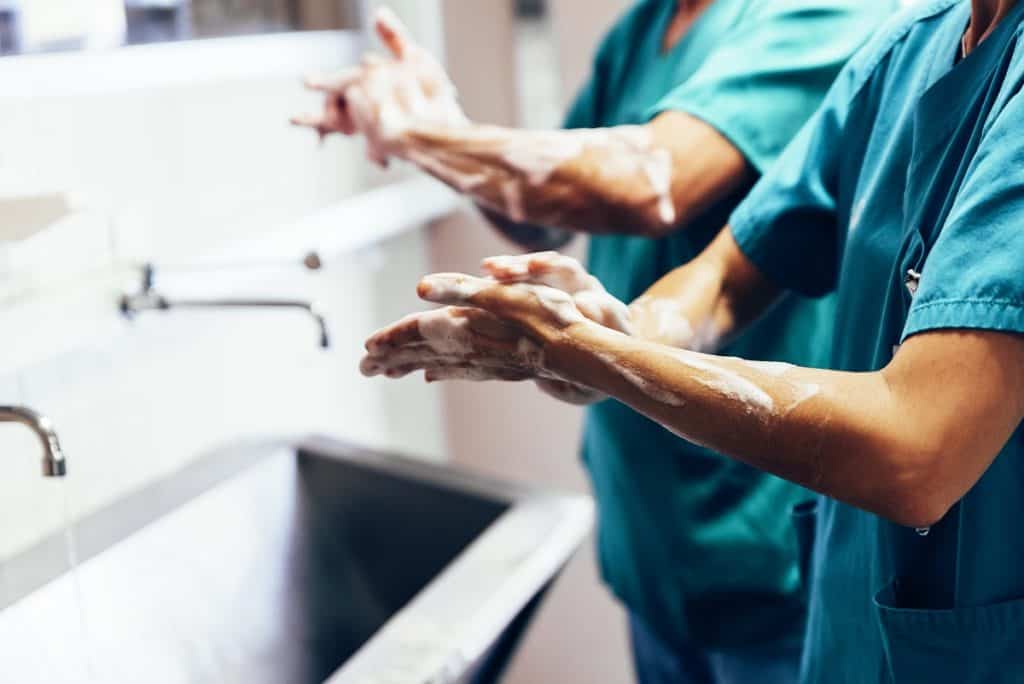 Medical professionals scrubbing in at a sink.