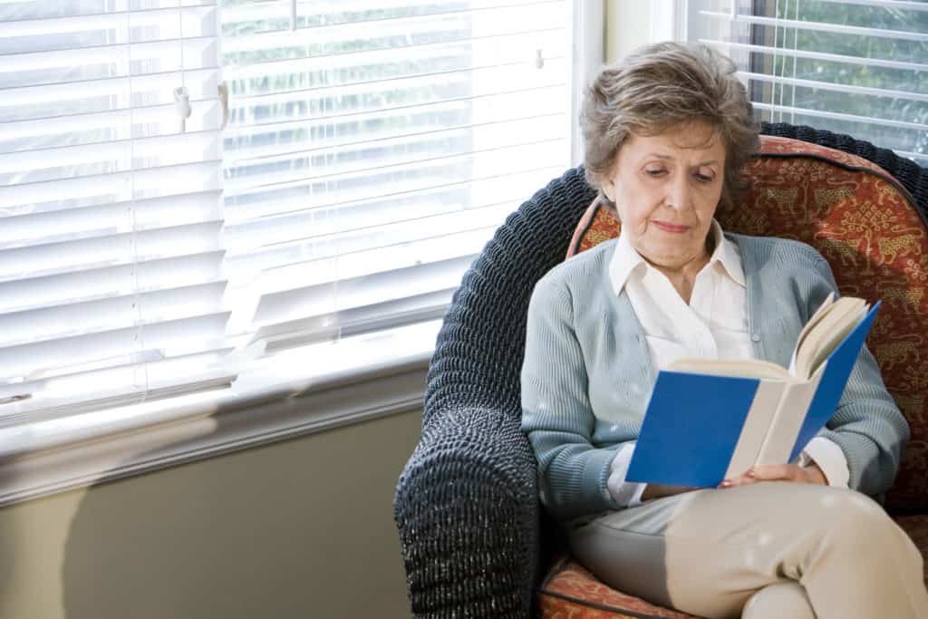 A senior woman reading a book in an armchair.