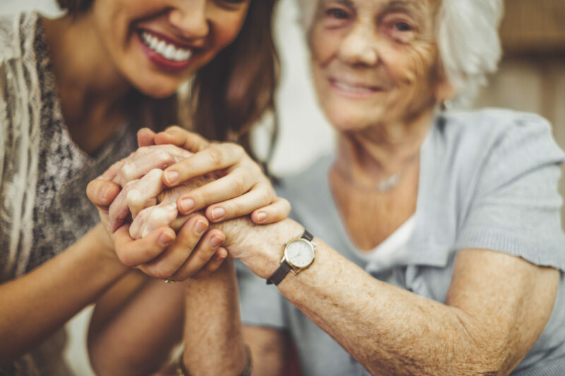 Close-up of a smiling nurse holding a senior woman's hand