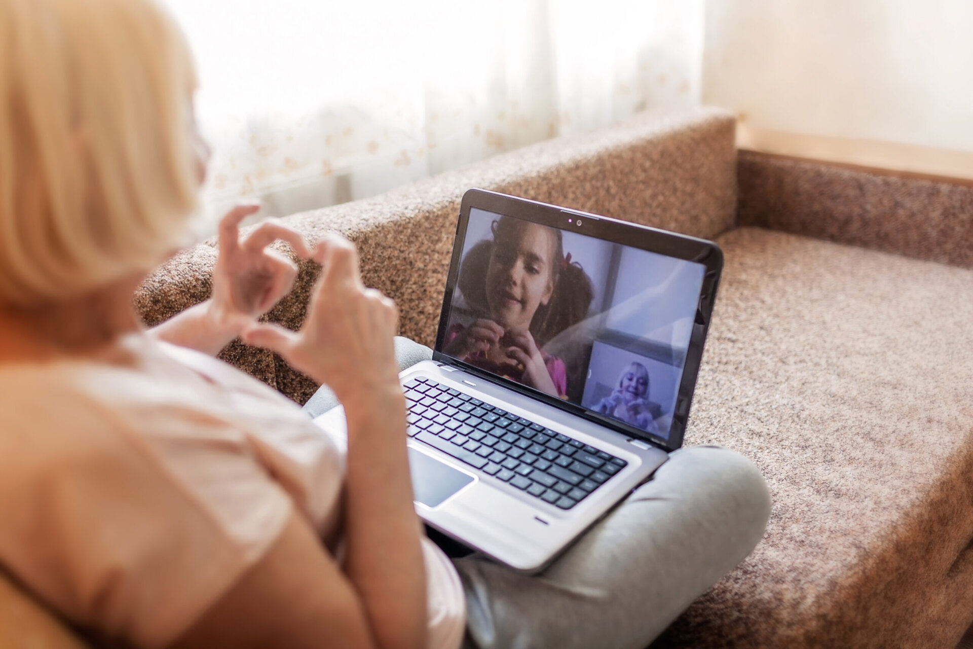 Senior woman sitting on a couch talking with grandchild on laptop screen