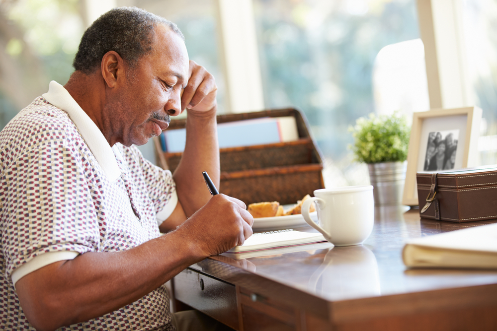A senior man sites down at a desk to write in a journal