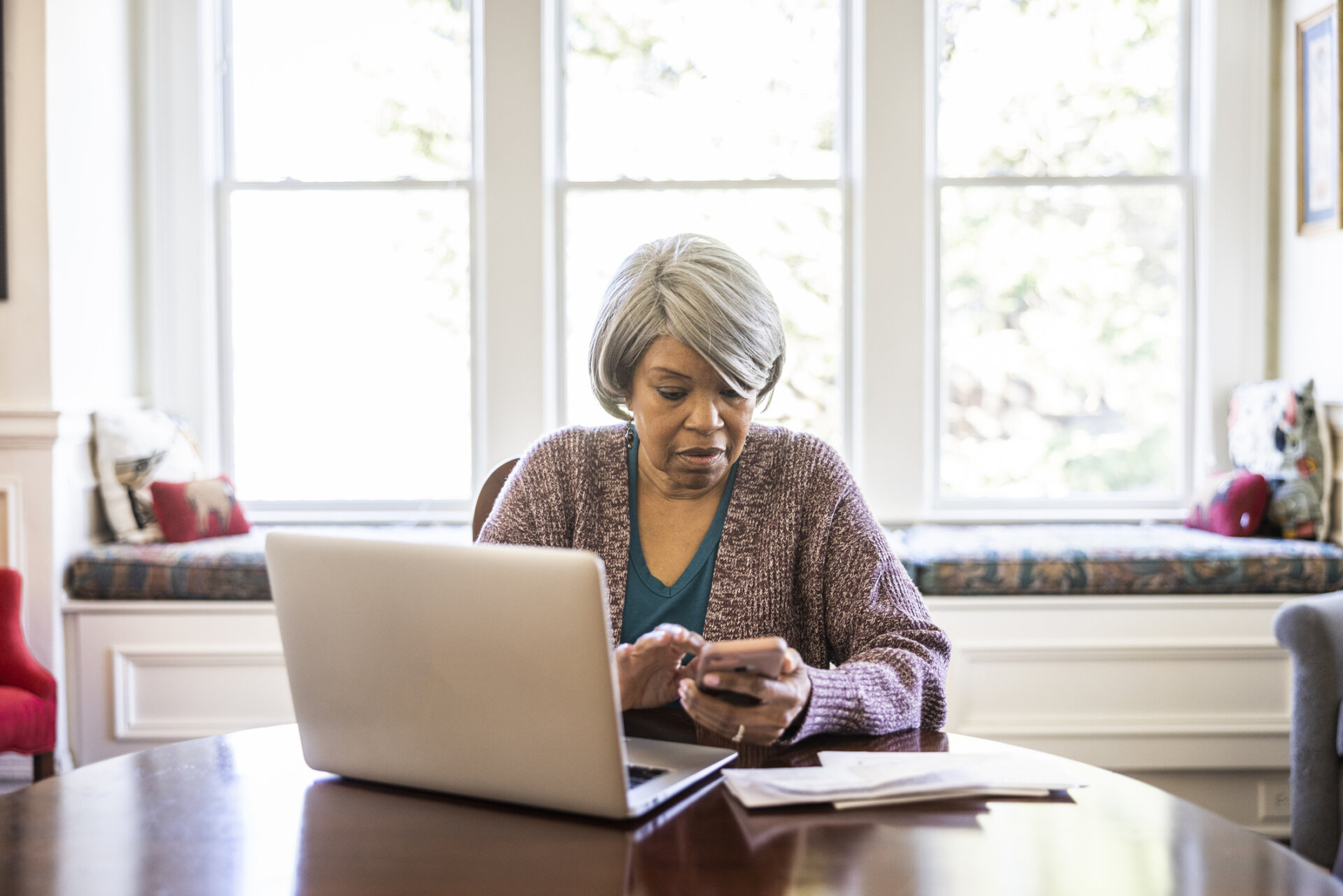 A woman looking at paperwork at her phone and laptop