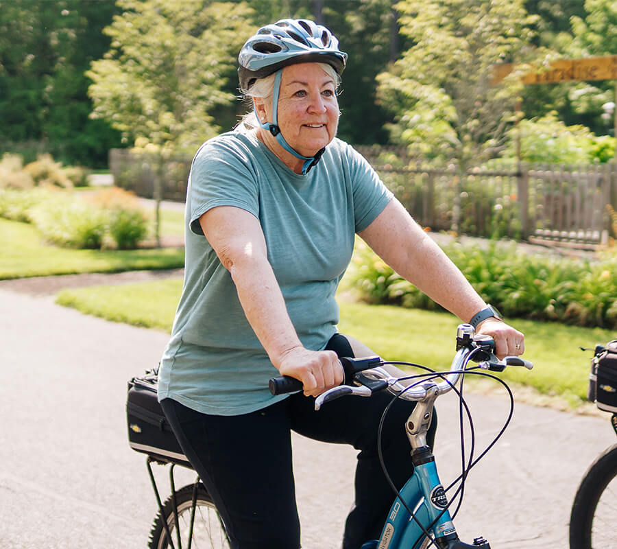 Woman in a helmet biking on a sunny path beside lush greenery.