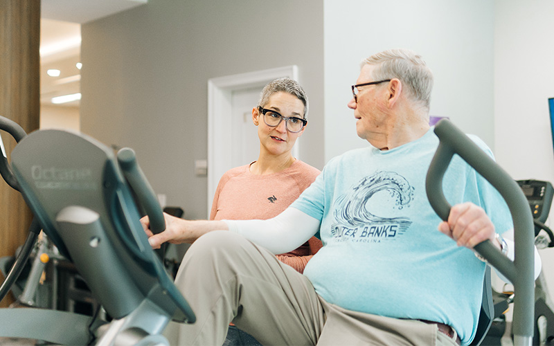 Two seniors exercising on stationary bikes in a community gym.