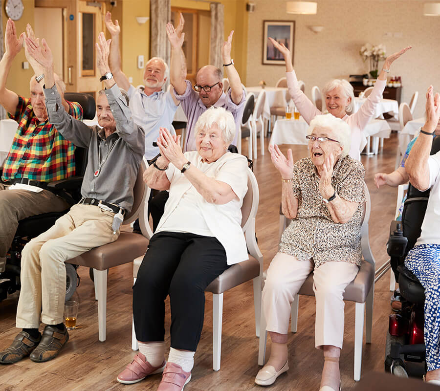 Group of seniors clapping and raising hands in bright common area.