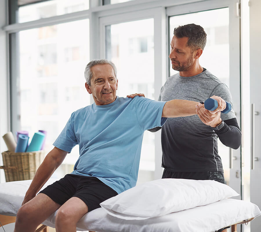 Senior man receiving shoulder exercise assistance from a therapist in a bright room.