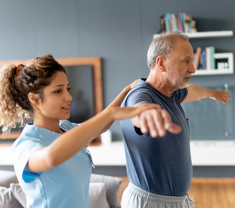 Nurse assists elderly man with physical therapy exercises at a living unit.