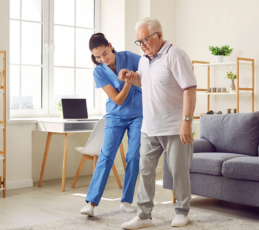 Caregiver assisting senior man with walking in a bright, cozy living unit.