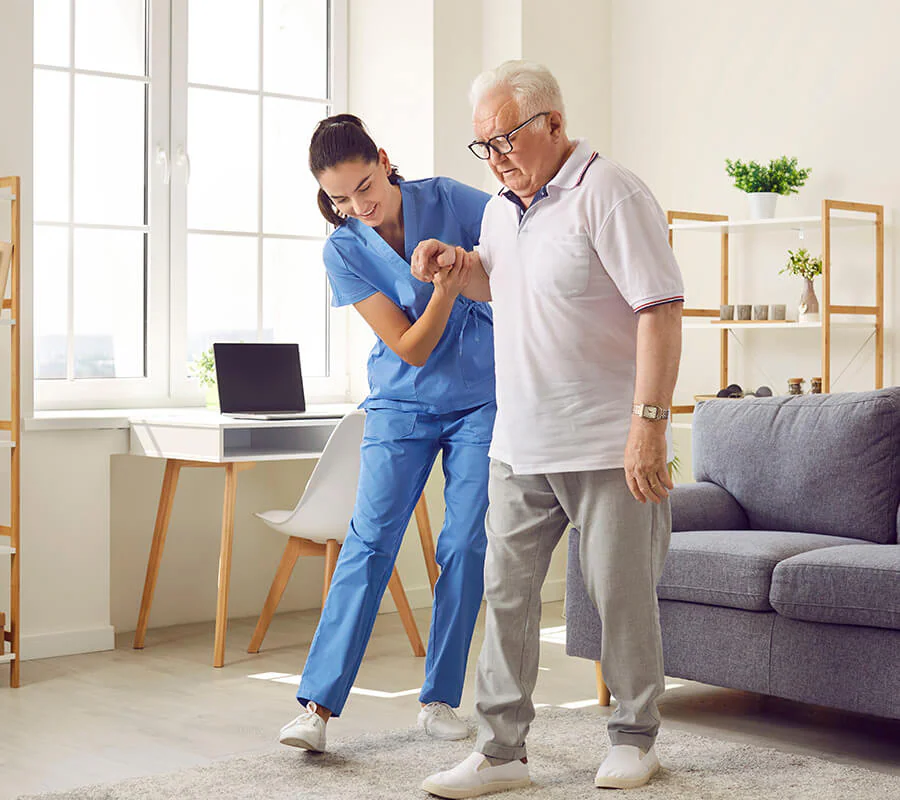 Caregiver assisting senior man with walking in a bright, cozy living unit.