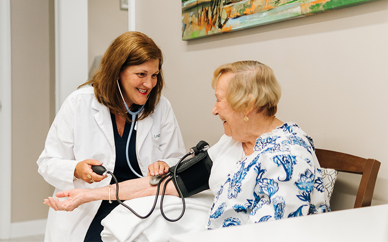 Caregiver checking blood pressure of a smiling senior woman in a cozy unit setting.