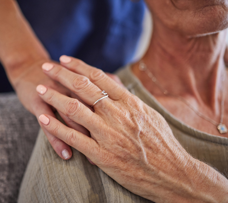 Close-up of a caregivers hand gently resting on an elderly womans shoulder.