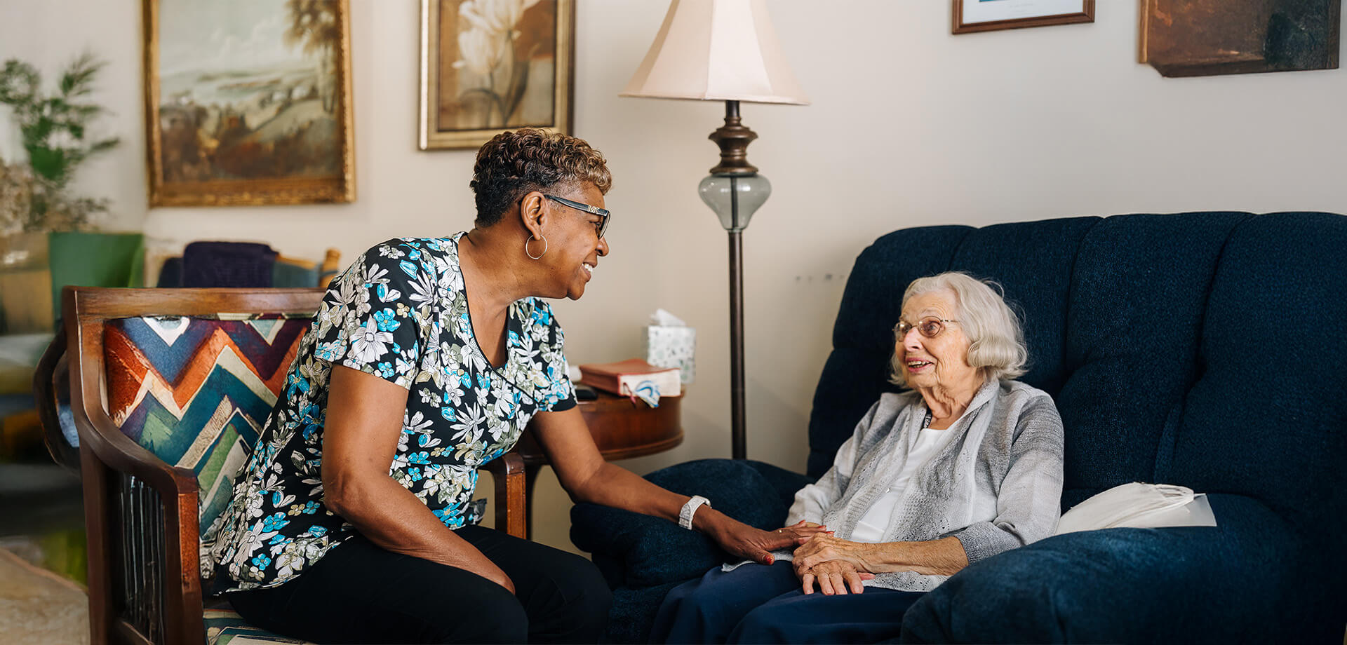 Smiling caregiver and elderly woman enjoying a moment at a table in a communal space.