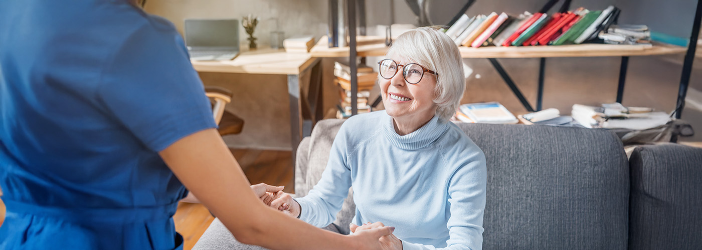 Smiling senior woman holding hands with caregiver in a cozy room.