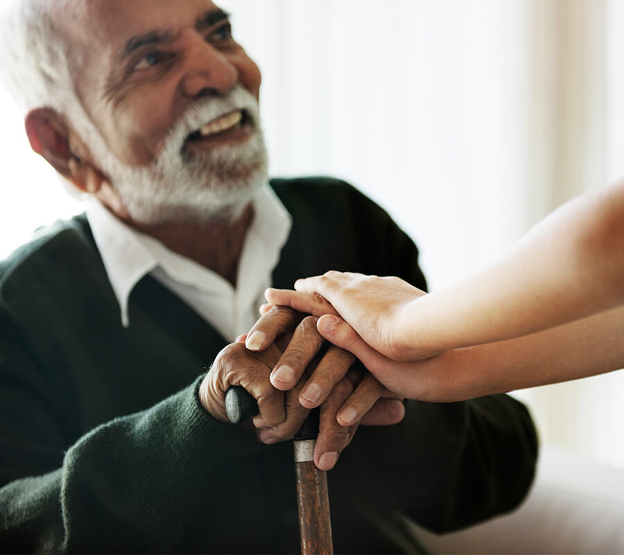 Elderly man smiling while holding hands with a supportive person.