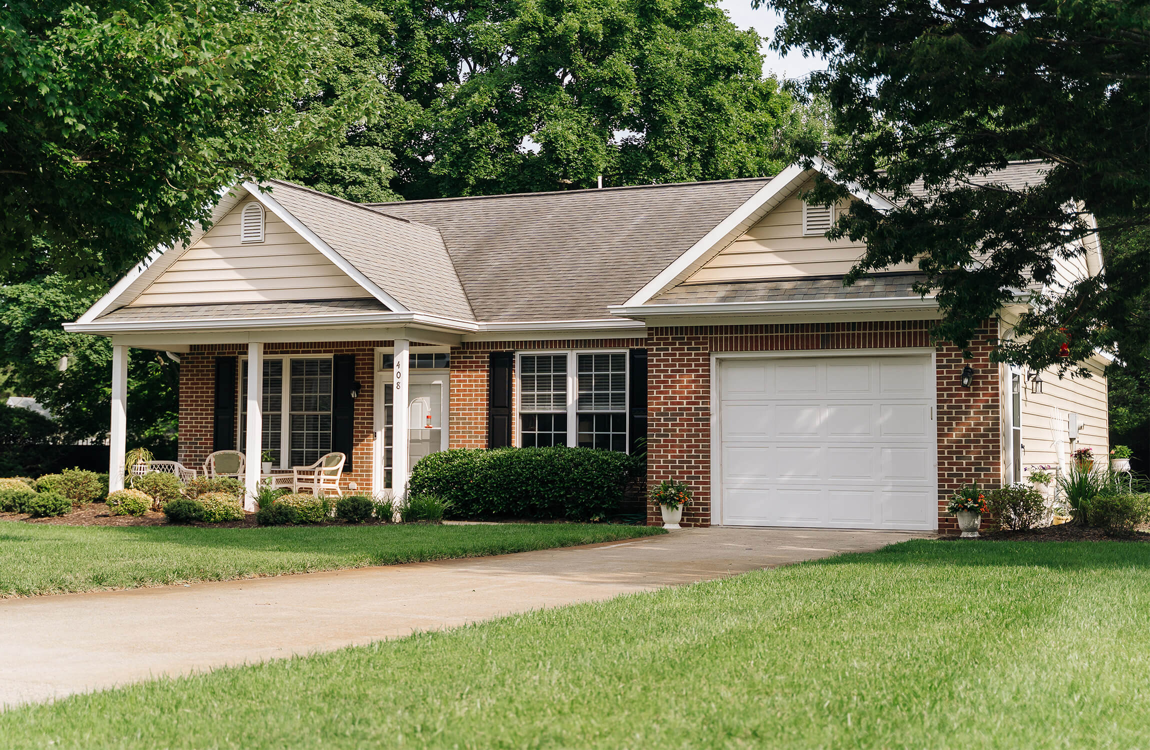 Brick and siding unit with porch in a mature tree setting.