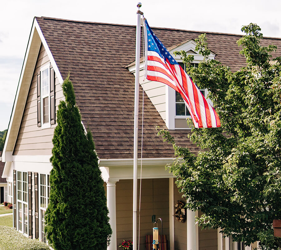 American flag waves near unit with sloped roof and greenery in front.