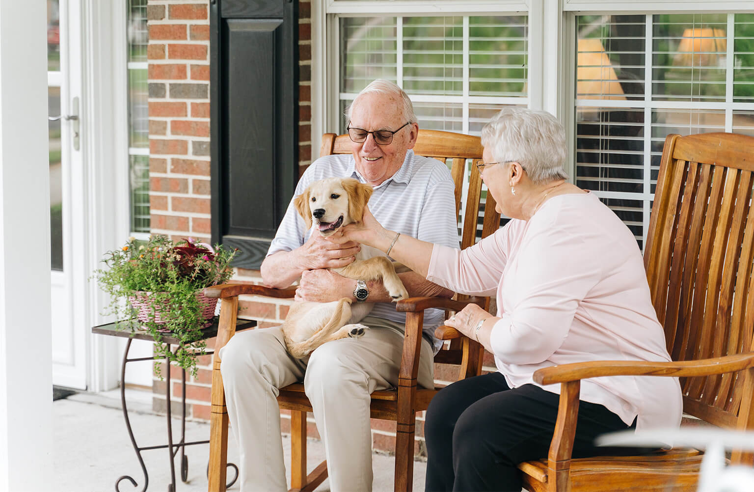 Senior couple plays with cute puppy on their porch