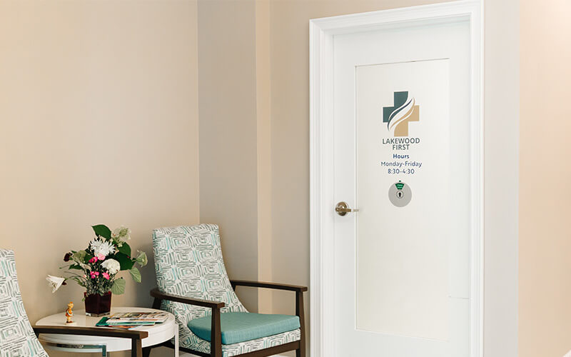 Comfortable Waiting Area with Door Signage Waiting area with two chairs and flowers near a door with a logo and business hours.