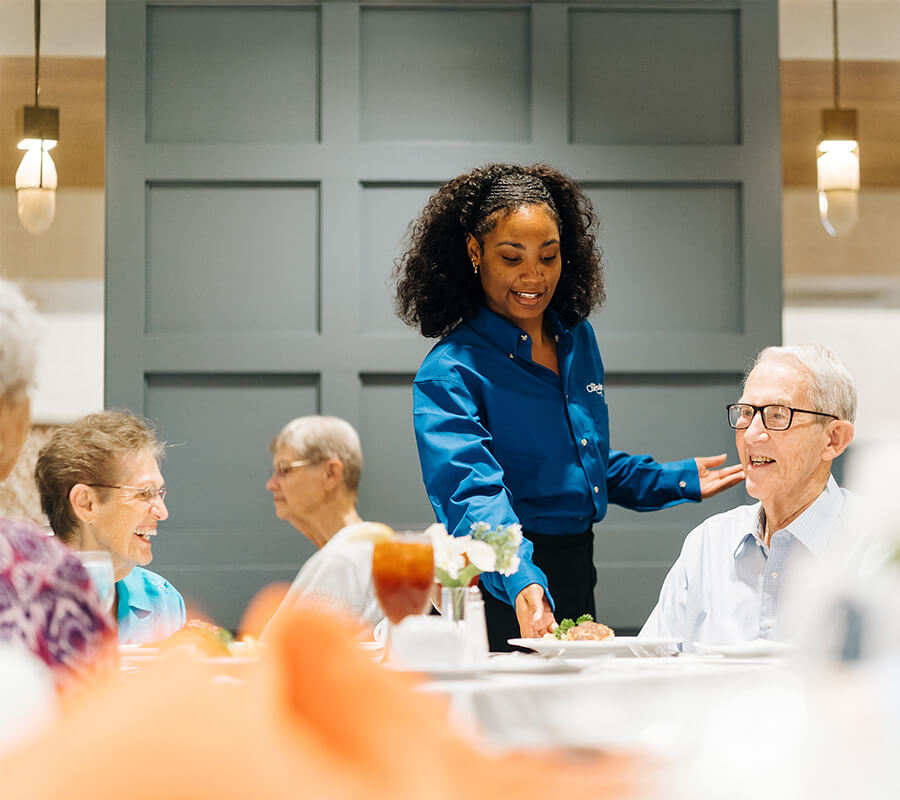 Social Dining in Community Senior women enjoying a meal together at a dining area in a lively community setting.