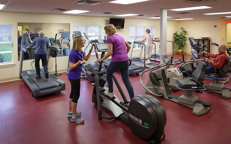 Residents exercising in a fitness center with treadmills and stationary bikes.