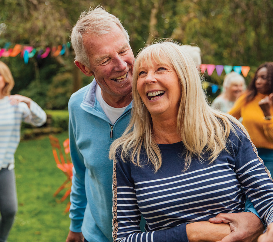 Smiling seniors enjoying an outdoor event in a community garden with colorful banners.