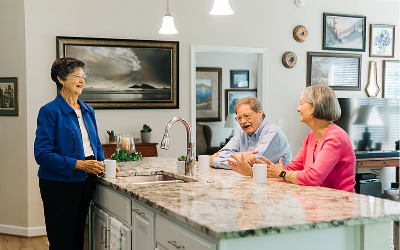 Friendly Chat in Community Kitchen Three seniors enjoy a conversation in a bright and modern kitchen area.