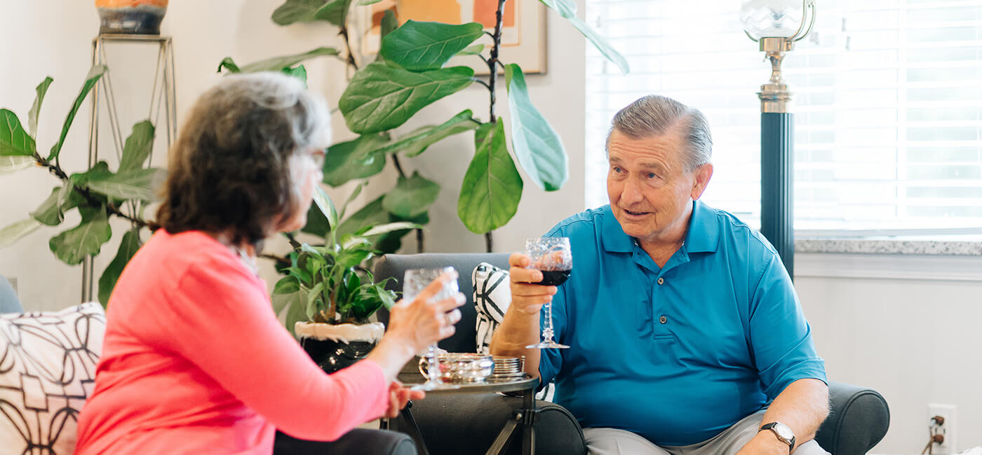 Two seniors enjoying drinks and conversation in a bright community lounge.