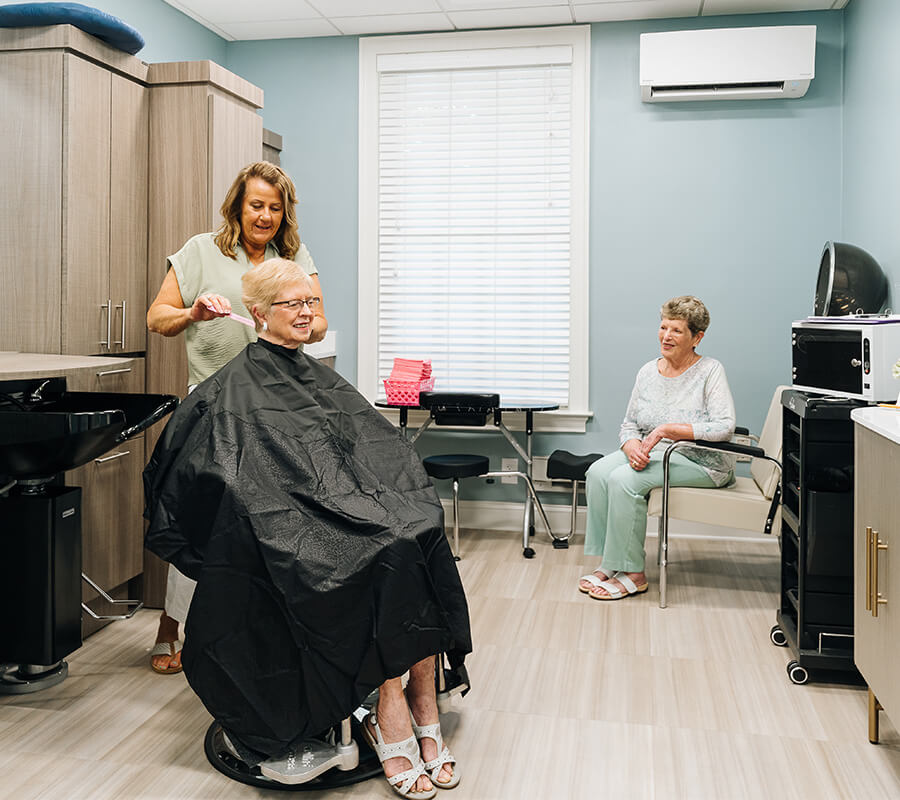 Two seniors receiving hairdressing services in community salon area.