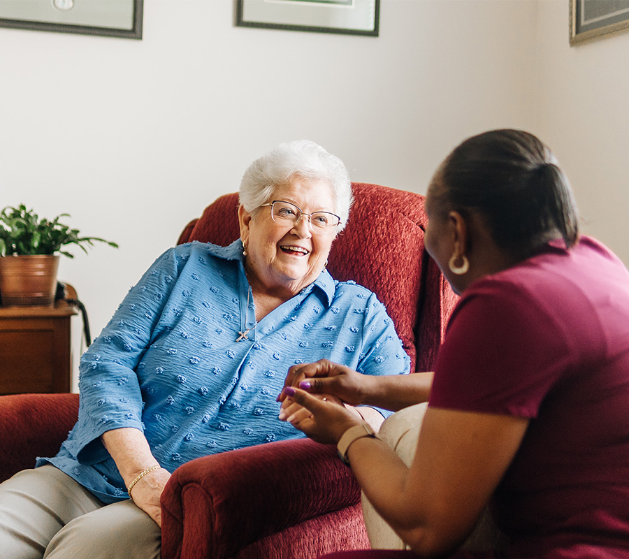 Smiling elderly woman sharing a conversation with a caregiver in a cozy living unit.