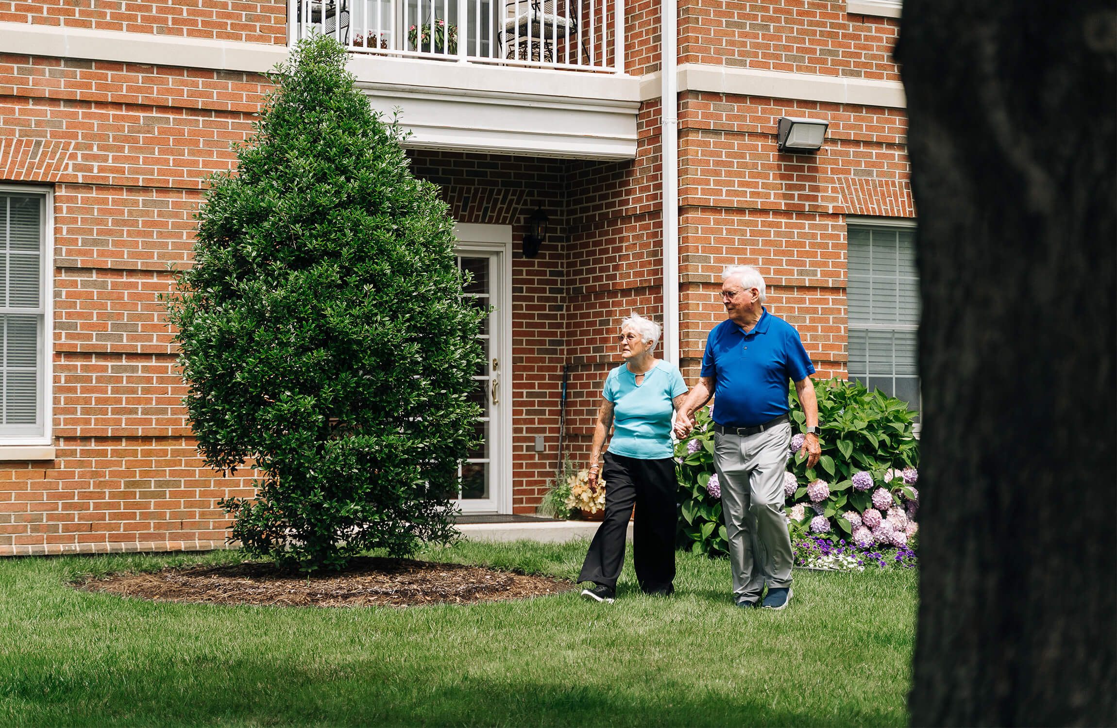 Elderly couple walking outside a brick senior living community.