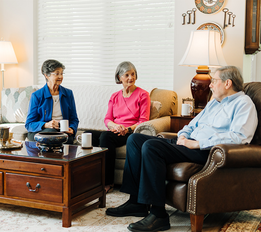 Three seniors sitting together in a cozy living room sharing coffee and conversation.
