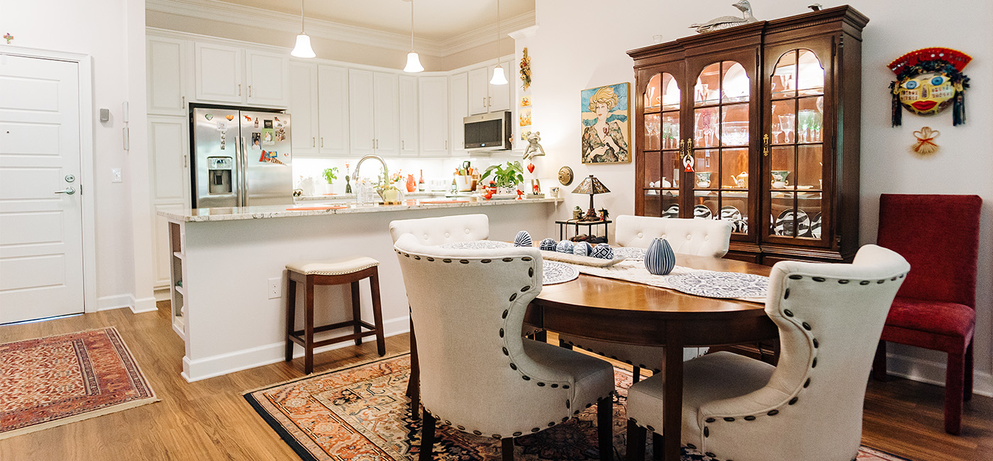 Cozy dining area with wooden furniture and open-plan kitchen in a senior living unit.
