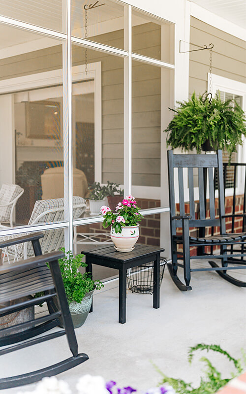 Cozy porch with rocking chairs, plants, and a small table with flowers.