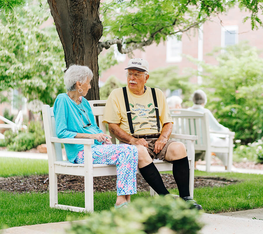 Elderly couple sitting on a bench in a garden at a senior living community.