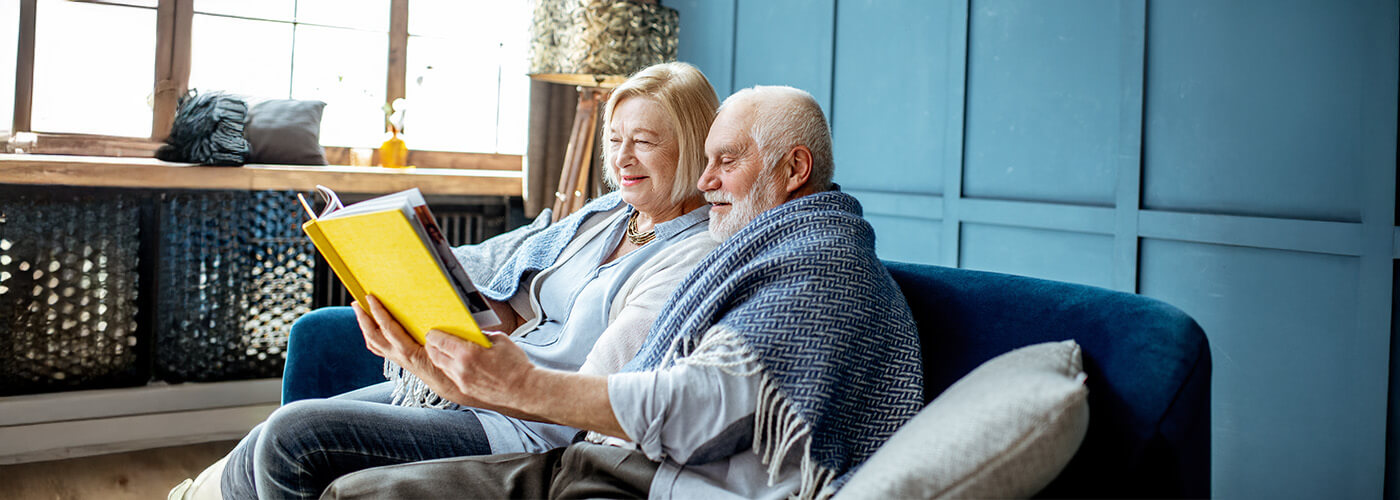 Elderly couple reading a book together in a cozy living room area.