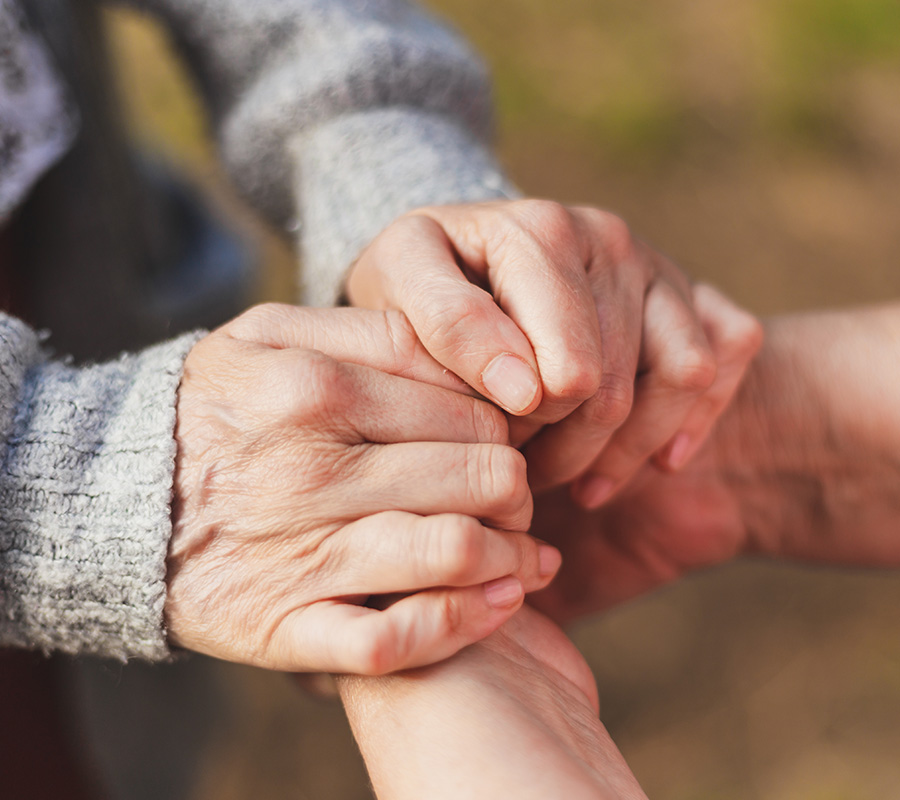 Elderly hands gently holding another persons hand outdoors.