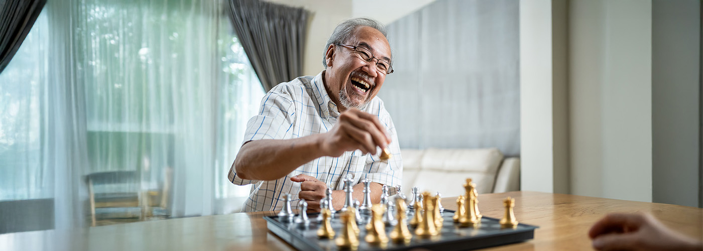 Smiling elderly man playing chess in a bright, cozy living space.