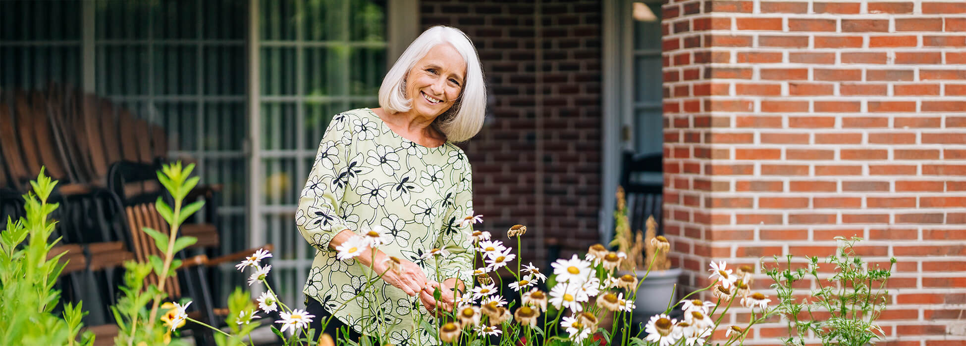 Smiling elderly woman tending flowers outside her unit in senior community.