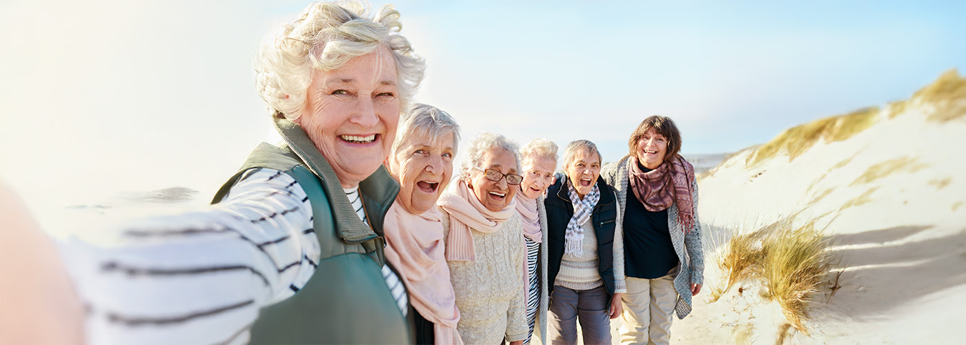 A group of elderly women smiling and walking on a sandy beach.