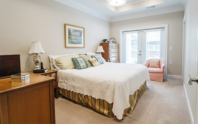 Elegant Bedroom in Senior Unit Elegant bedroom in a senior living community with a bed, dresser, and cozy chair.