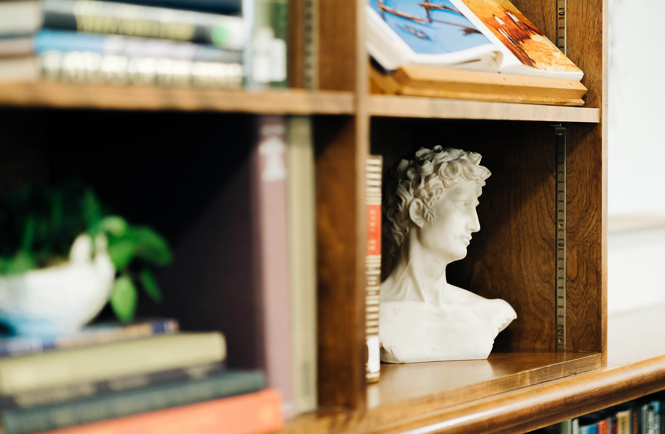 Bookshelf with books, plant, and small bust sculpture in a senior living unit.