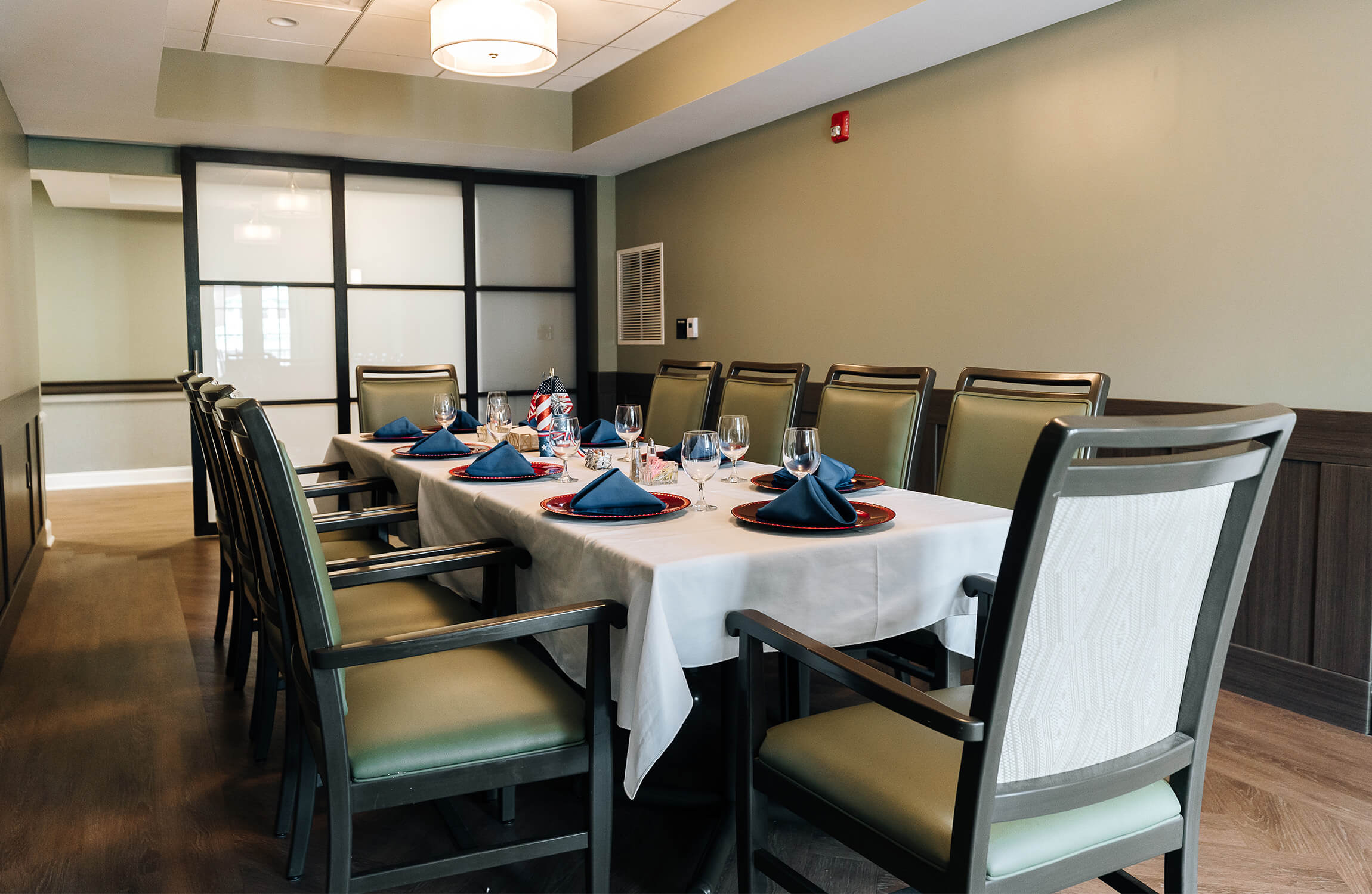 Elegant dining room with set table, blue napkins, and green cushioned chairs in a living unit.