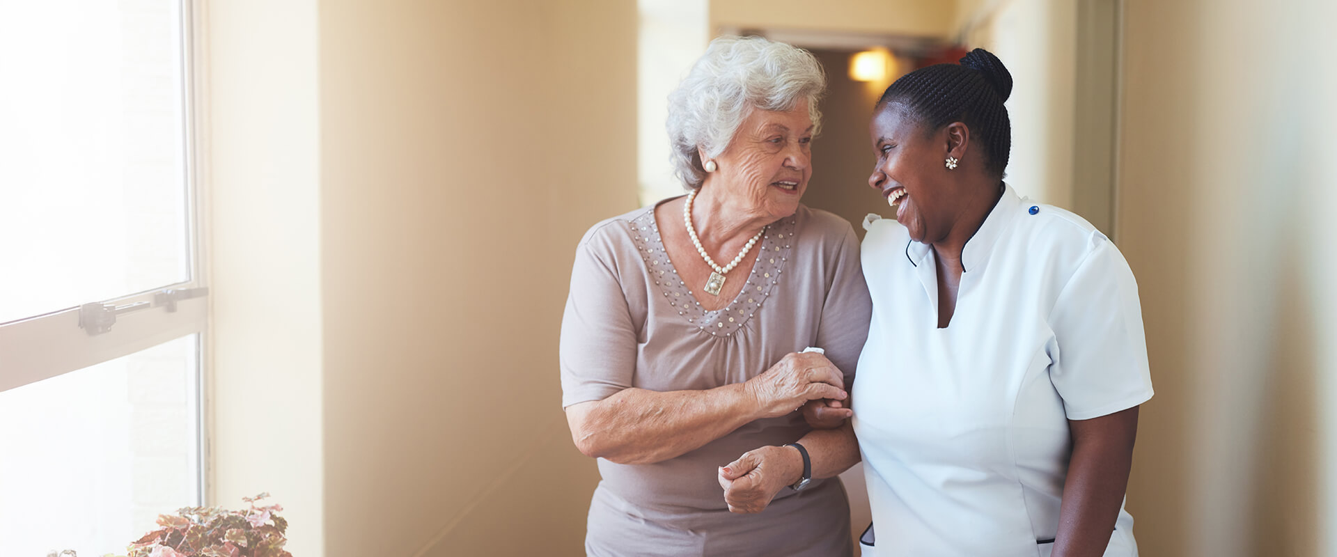 employee helping a senior woman walk down a hallway