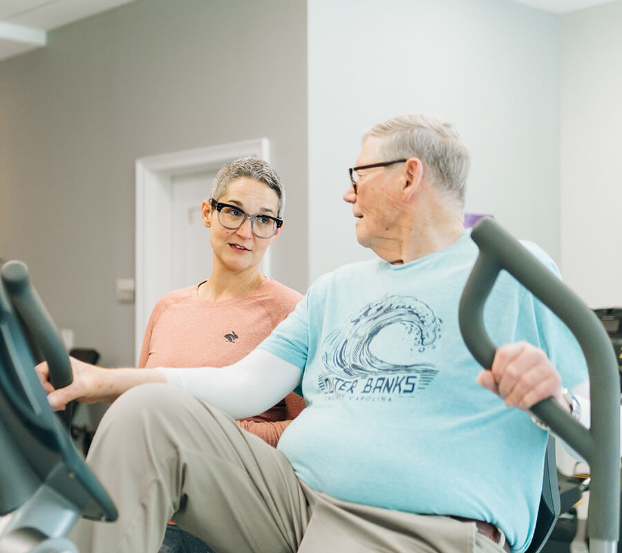 Older man and woman chatting while using exercise equipment in a wellness center.