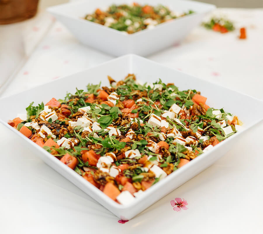Fresh salad with arugula, feta, walnuts, and dressing in a white square bowl.