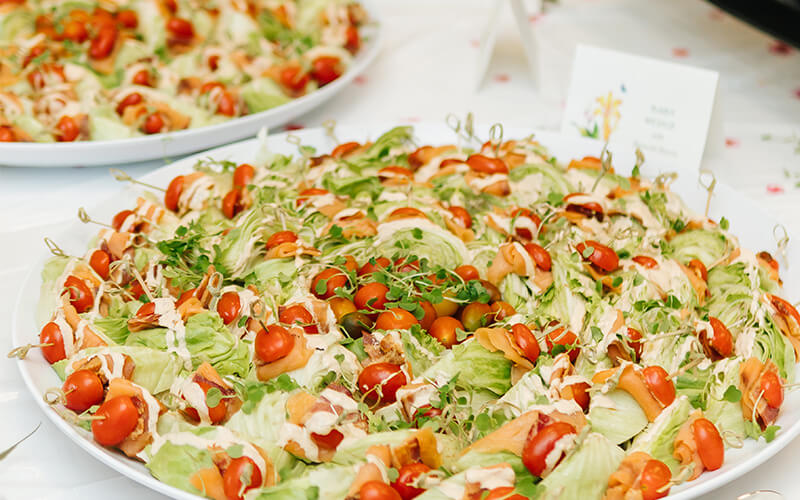Platters of salad with lettuce, cherry tomatoes, sprouts, and dressing on a dining table.