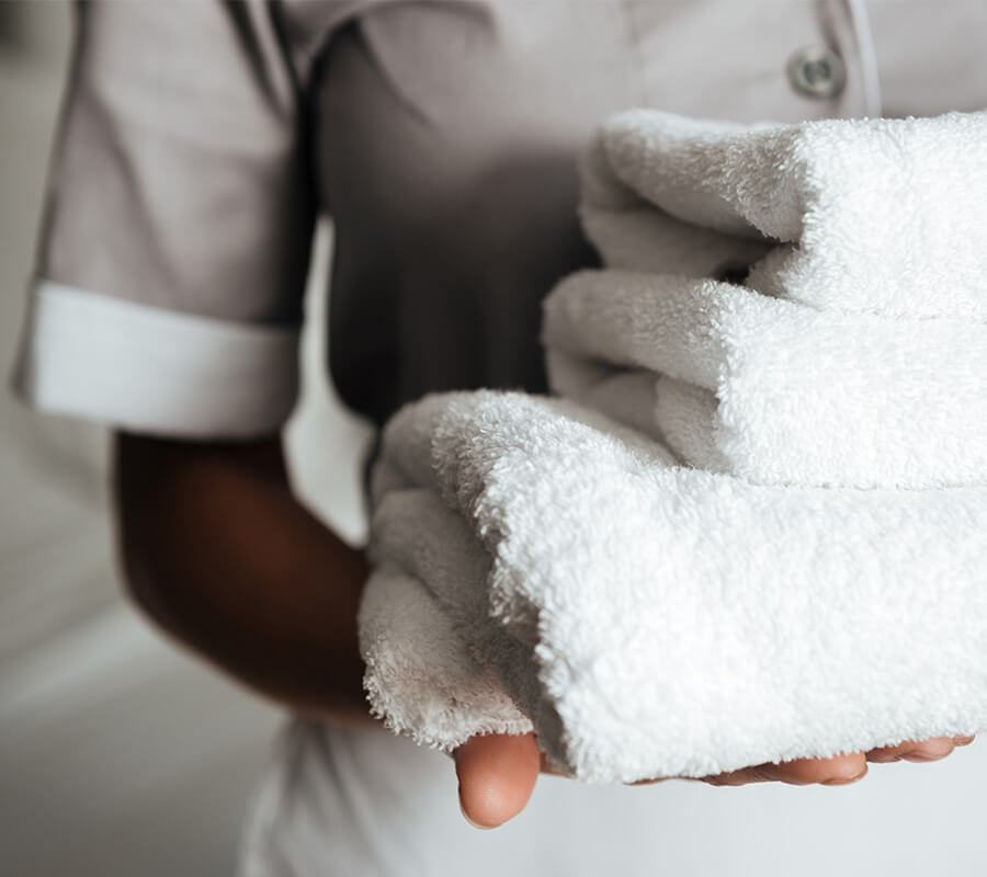 Person holding a stack of neatly folded white towels in a welcoming setting.