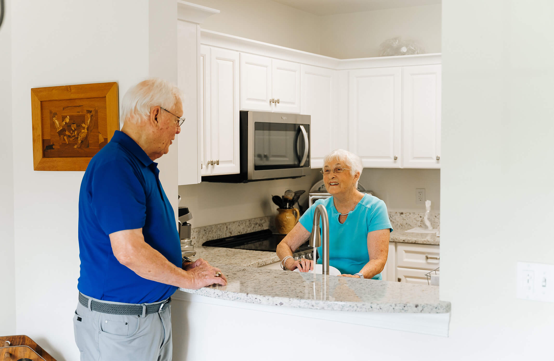 Elderly couple talking in a bright kitchen within a senior living unit.