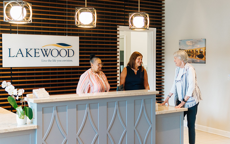 Three women talking at the reception desk of a senior living community.