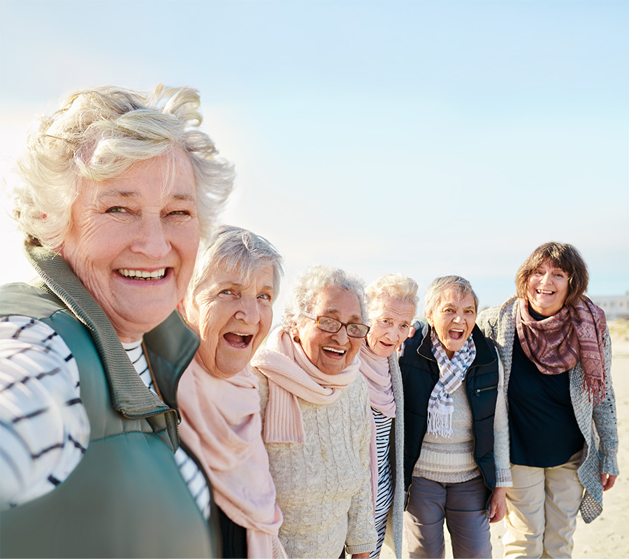 Group of six smiling seniors enjoying a day at the beach together.